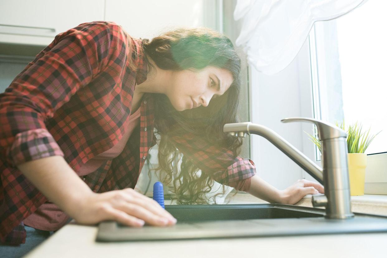 Serious concentrated young woman in checkered shirt checking tap while having trouble dropping the tap in the kitchen