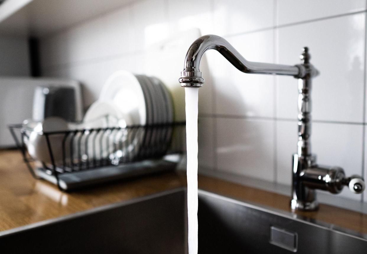 Water flows from a stainless steel kitchen faucet down the sink. Wasting water by running a chrome faucet. Using excessive household water. Water misuse in household chores and activities.