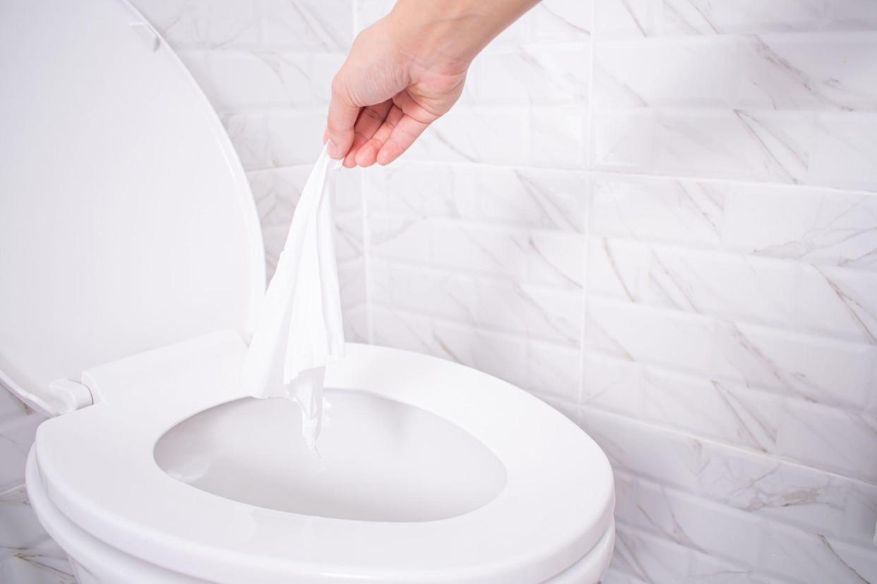 Close-up hand throwing toilet paper to the toilet in a white tile bathroom.