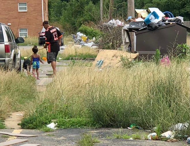 On Friday, a man leads a little girl and a dog through trash and tall grass in the apartments of Colonial Village, an East Side complex that the city has taken to court to clean it up.